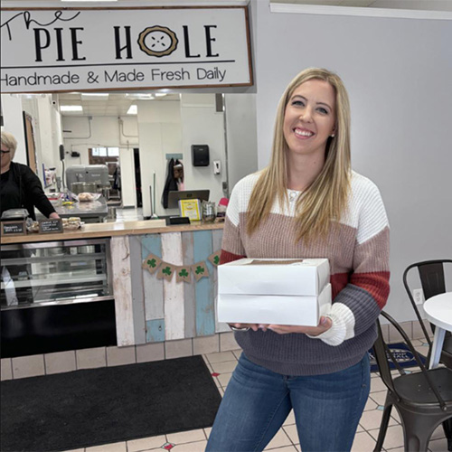 Blond woman smiles while holding two pie boxes in local evanston, wy shop: The Pie Hole>