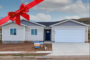 craftsman style tan white and grey home with blue sky and clouds behind it. red ribbon bow is across the corner of the photo