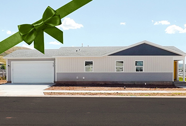 Single story home with two-car garage in Evanston, WY with tan, grey, white, and blue accents. A pale blue sky with a handful of clouds is in the distance with a hint of the rolling foothills.