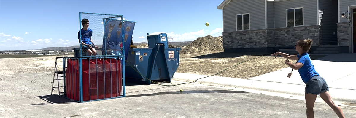 teenager sitting on a dunk tank about ready to fall in the water. girl throws ball at the target