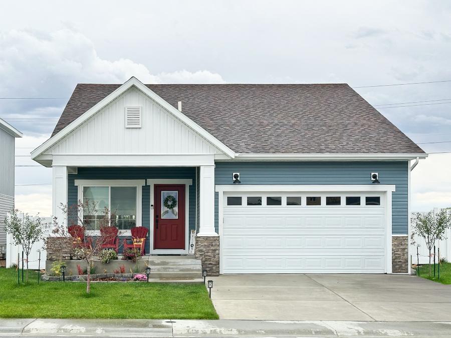 Quaint, farmhouse-style single story home with a spacious front porch, two car garage, and large front window.