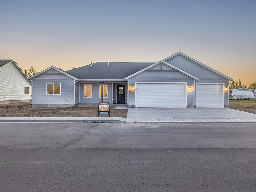 Evening Photo of Lovely Ranch home with grey blue siding, front porch with wreath on the door. Sunset in the background.